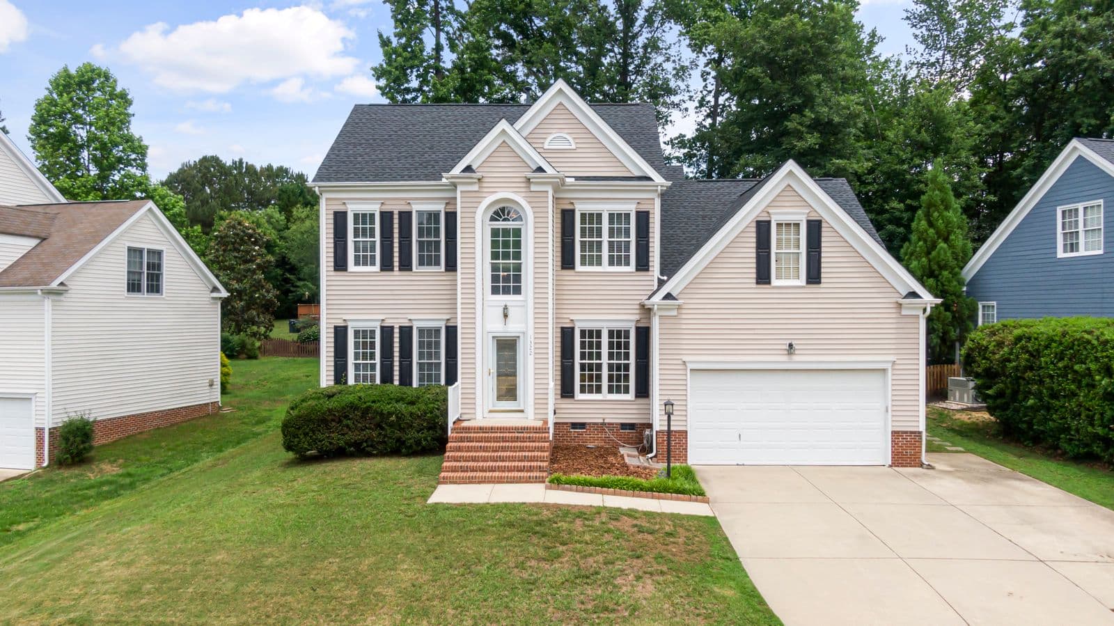 Two-story house with tan siding, black shutters and a two-car garage